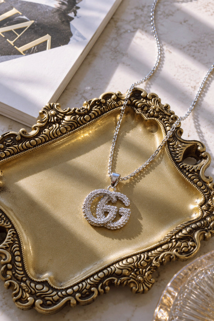 Silver crystal pendant necklace styled on an ornate gold tray with a fashion book.