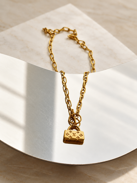 Petite Maison gold handbag charm necklace displayed alone on a curved mirror