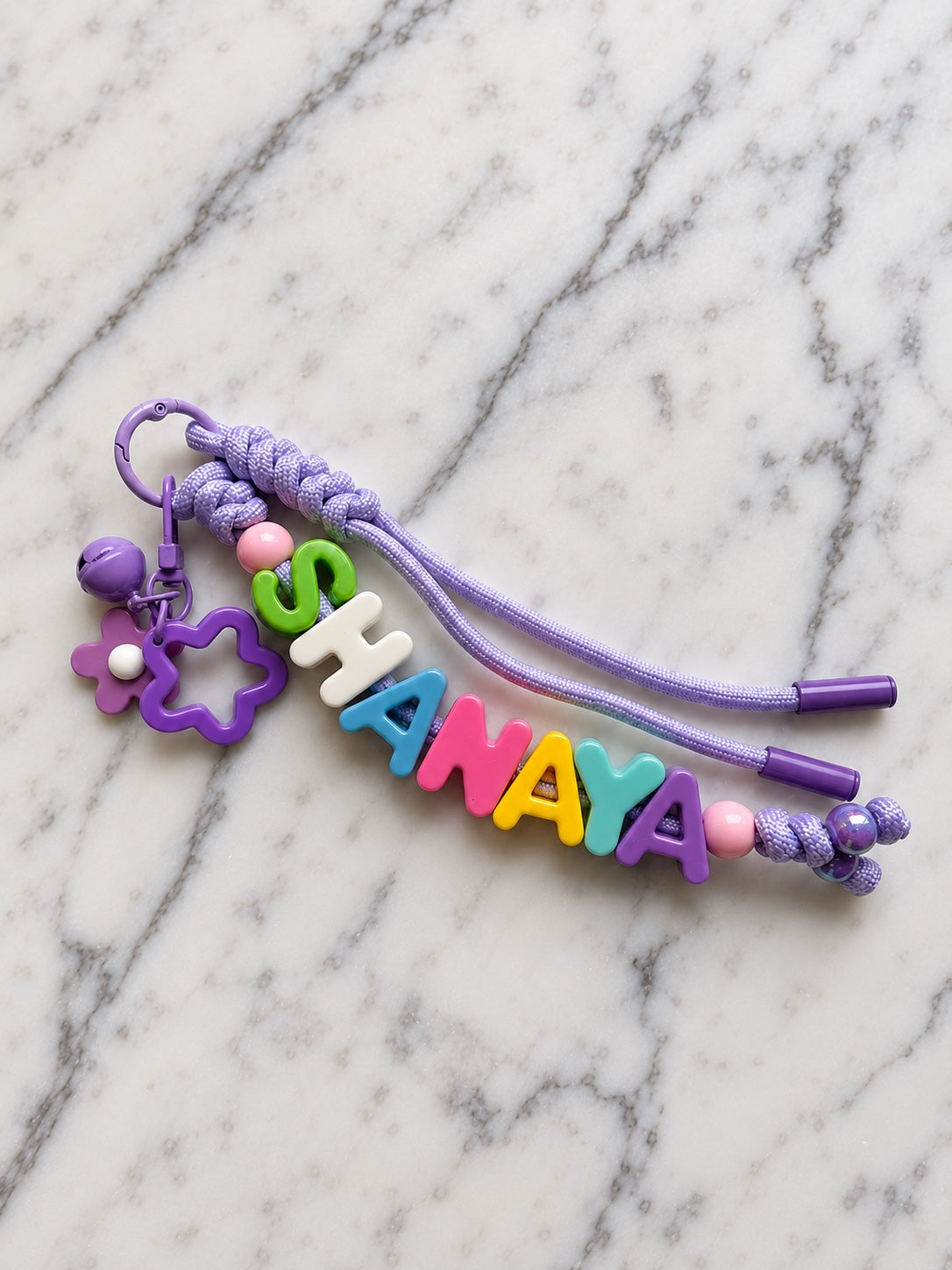 Purple cord and coordinated hardware name keychain with multicolored letter beads; SHANAYA is a personalization example