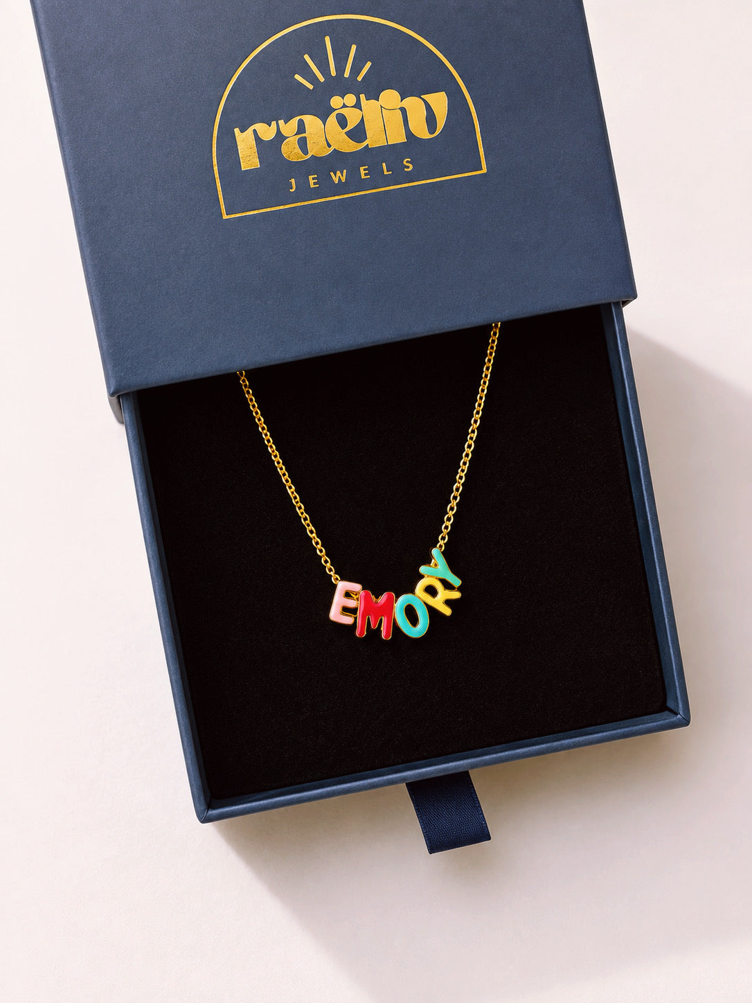 Gold-tone chain necklace with multicolored EMORY letter charms in a RAËLIV jewelry box; EMORY is a personalization example