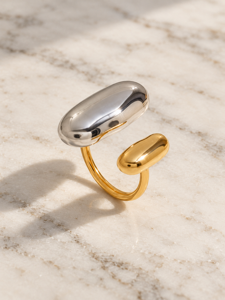 Two-tone sculptural open ring with a silver-tone elongated dome and smaller gold dome on warm pale marble