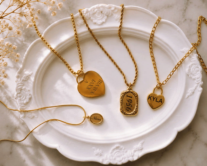 Personalized gold keepsake necklaces with name, date and Nana engravings on a vintage white plate.