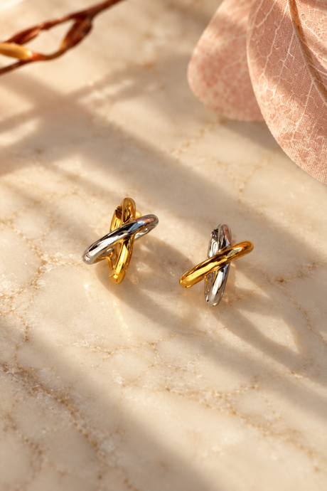 Pair of petite gold and silver crossover huggie earrings in warm sunlight